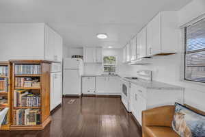 Kitchen with a sink, dark wood-style floors, white cabinetry, white appliances, and light stone countertops