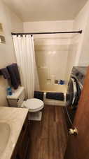 Bathroom with toilet, vanity, wood finished floors, shower / bath combination with curtain, and washer / clothes dryer