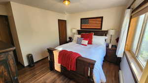 Bedroom with a baseboard heating unit, multiple windows, wood finished floors, and a textured ceiling