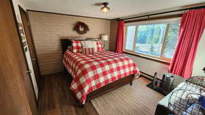 Bedroom featuring a textured ceiling, baseboard heating, wood finished floors, and brick wall