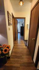 Corridor with dark wood-type flooring, baseboards, and a textured ceiling