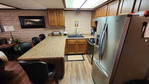 Kitchen with brick wall, light wood finished floors, a peninsula, a sink, and stainless steel appliances