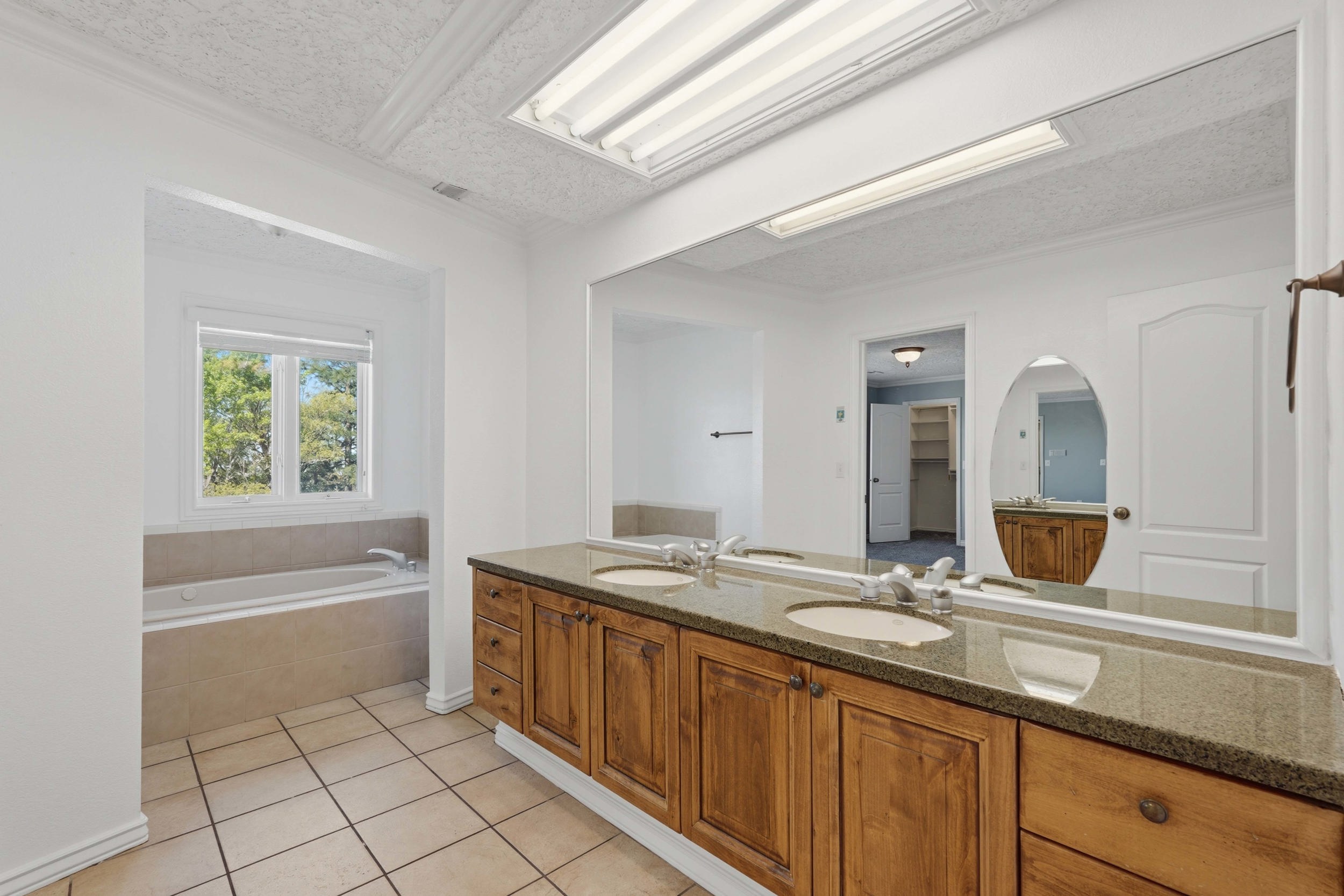 Full bath with double vanity, a bath, a textured ceiling, and light tile patterned floors