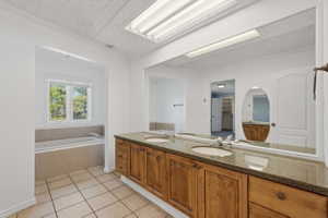 Full bath with double vanity, a bath, a textured ceiling, and light tile patterned floors
