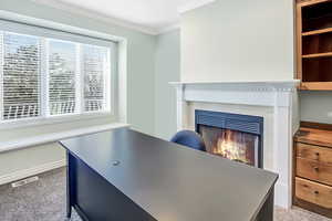 Carpeted office space with visible vents, crown molding, and a lit fireplace