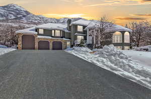 View of front of property with a mountain view, stone siding, a chimney, and driveway