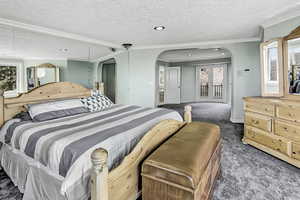 Bedroom featuring arched walkways, a textured ceiling, ornamental molding, and carpet flooring