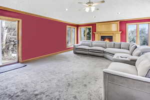 Carpeted living room with ceiling fan, baseboards, recessed lighting, a warm lit fireplace, and a textured ceiling