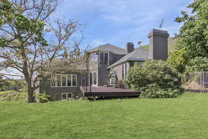 Back of house featuring a chimney, a lawn, a wooden deck, and fence