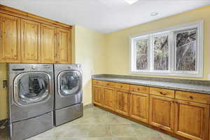 Laundry area with light tile patterned floors, washing machine and dryer, and cabinet space