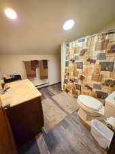 Full bath with a baseboard heating unit, toilet, vaulted ceiling, wood finished floors, and vanity