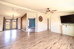 Unfurnished living room with ceiling fan with notable chandelier, french doors, wood finished floors, and lofted ceiling