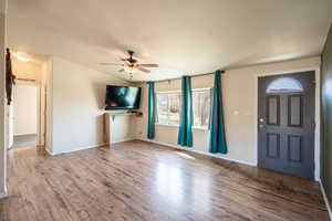 Unfurnished living room featuring vaulted ceiling, wood finished floors, a ceiling fan, and baseboards