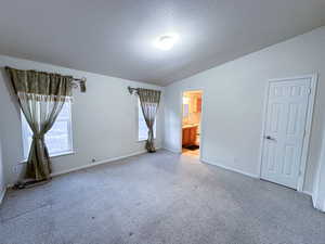 Unfurnished bedroom with lofted ceiling, ensuite bath, a textured ceiling, carpet flooring, and multiple windows