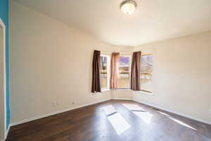 Empty room featuring dark wood-style flooring, visible vents, and baseboards