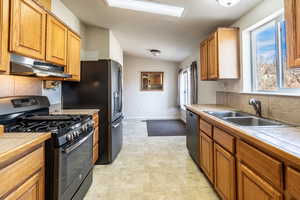 Kitchen with tile countertops, a sink, stainless steel gas range, under cabinet range hood, and dishwashing machine