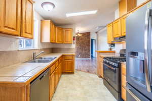 Kitchen featuring tile countertops, under cabinet range hood, stainless steel appliances, a sink, and light floors