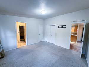 Unfurnished bedroom featuring ensuite bathroom, carpet flooring, and a textured ceiling