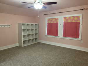 Carpeted empty room featuring vaulted ceiling, baseboards, and ceiling fan