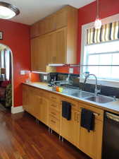 Kitchen with dark wood-type flooring, pendant lighting, black dishwasher, arched walkways, and a sink