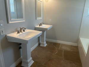 Full bathroom with baseboards, stone tile floors, two sinks, and a washtub