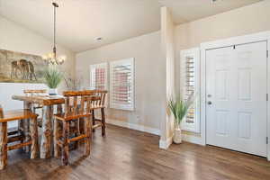 Dining space with wood finished floors, baseboards, visible vents, lofted ceiling, and a chandelier