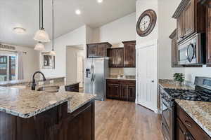 Kitchen with dark brown cabinets, pendant lighting, light wood-type flooring, appliances with stainless steel finishes, and a sink