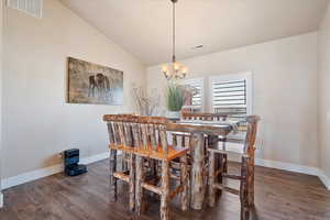 Dining area with a chandelier, visible vents, wood finished floors, and vaulted ceiling