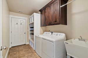 Laundry area featuring visible vents, washer and clothes dryer, a sink, stone finish flooring, and cabinet space