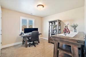 Home office featuring a textured ceiling, baseboards, visible vents, and light carpet