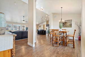 Dining space featuring visible vents, baseboards, ceiling fan with notable chandelier, wood finished floors, and high vaulted ceiling