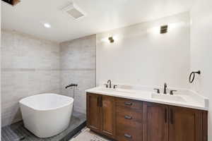 Bathroom featuring double vanity, a soaking tub, tile walls, and recessed lighting