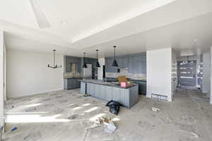 Kitchen featuring gray cabinetry, an island with sink, tasteful backsplash, and dark countertops