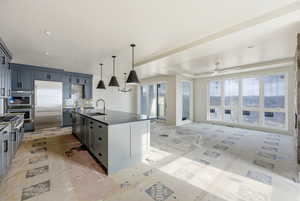 Kitchen featuring an island with sink, appliances with stainless steel finishes, gray cabinetry, open floor plan, and hanging light fixtures