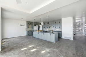 Kitchen with gray cabinetry, dark countertops, hanging lights, and a large island with sink