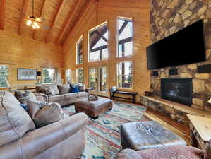 Living room featuring wood walls, hardwood / wood-style floors, a stone fireplace, wooden ceiling, and plenty of natural light