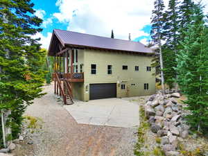 View of side of home featuring a deck, stairway, metal roof, concrete driveway, and a garage