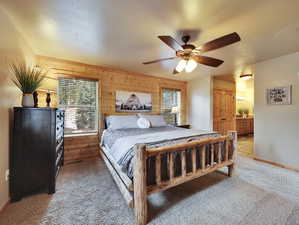 Carpeted bedroom featuring connected bathroom, baseboards, wooden walls, and ceiling fan