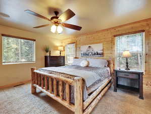 Carpeted bedroom with visible vents, multiple windows, and wood walls