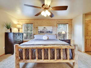 Bedroom with a ceiling fan, wooden walls, light colored carpet, and baseboards