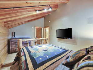 Carpeted bedroom featuring wood walls and lofted ceiling with beams