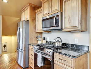 Kitchen featuring dark stone countertops, stainless steel appliances, and light brown cabinets