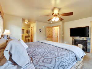 Carpeted bedroom featuring a tiled fireplace, ensuite bath, and ceiling fan
