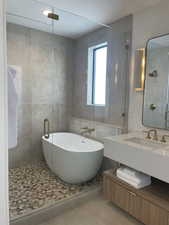 Full bath with tile patterned flooring, tile walls, a stall shower, a freestanding tub, and vanity