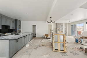 Kitchen with a sink, gray cabinets, stone countertops, and a kitchen island with sink