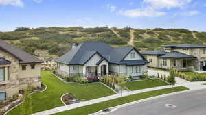 View of front of house with driveway, a chimney, a shingled roof, a front lawn, and stone siding