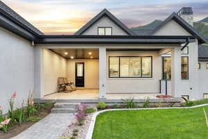 Exterior entry at dusk featuring covered porch, stucco siding, and a yard