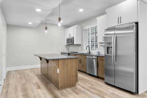 Kitchen featuring light wood finished floors, a sink, appliances with stainless steel finishes, dark countertops, and a center island