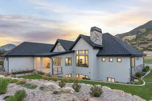 Back of property at dusk with stucco siding, a chimney, a mountain view, and a shingled roof