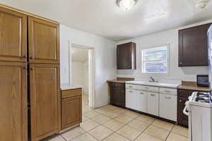 Kitchen with light tile patterned floors, gas range gas stove, a sink, light countertops, and a textured ceiling